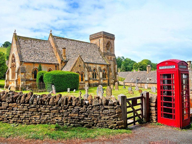 A Cotswold parish church behind a dry-stone wall with a red telephone box at the gate